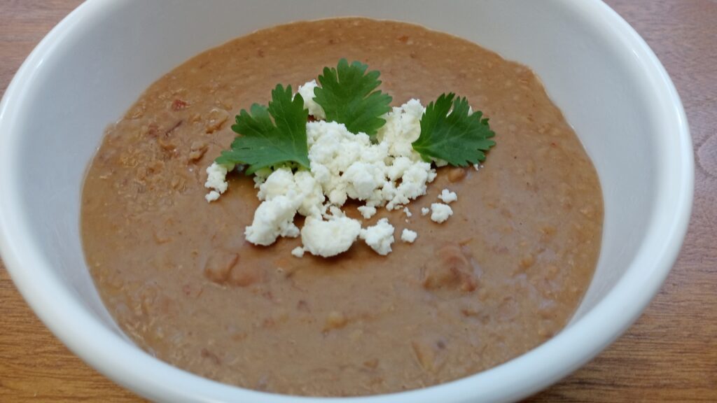 A bowl of refried beans made in the Instant Pot, topped with cilantro and queso cotija.
