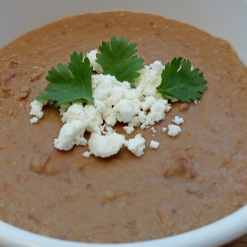 A bowl of refried beans made in the Instant Pot, topped with cilantro and queso cotija.