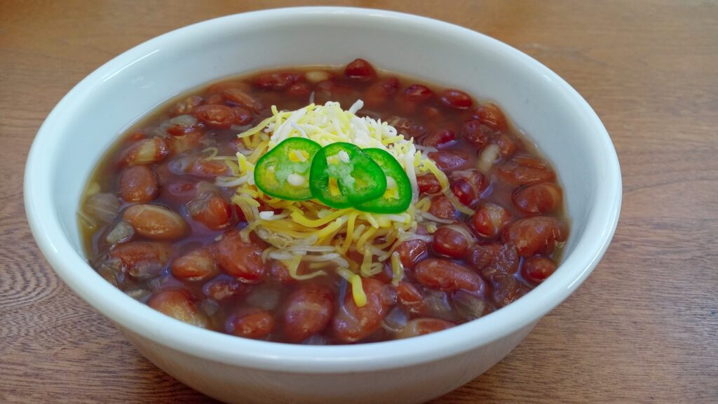 A delicious bowl of Chuckwagon Beans garnished with grated cheese and serrano pepper slices.